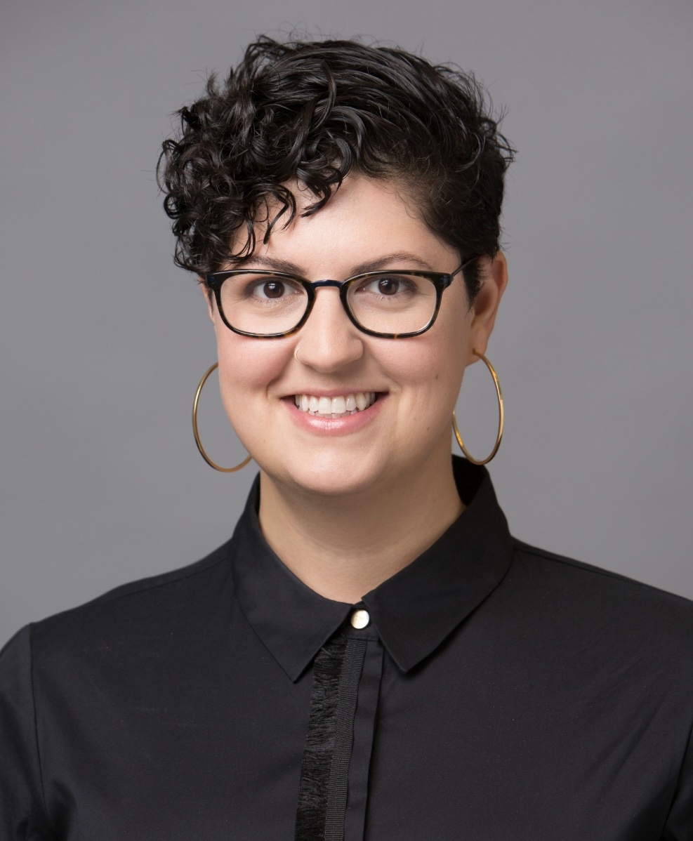 Picture of Dana Trocker, person with glasses, short curly dark hair, large gold hoop earrings, and a black button-up shirt